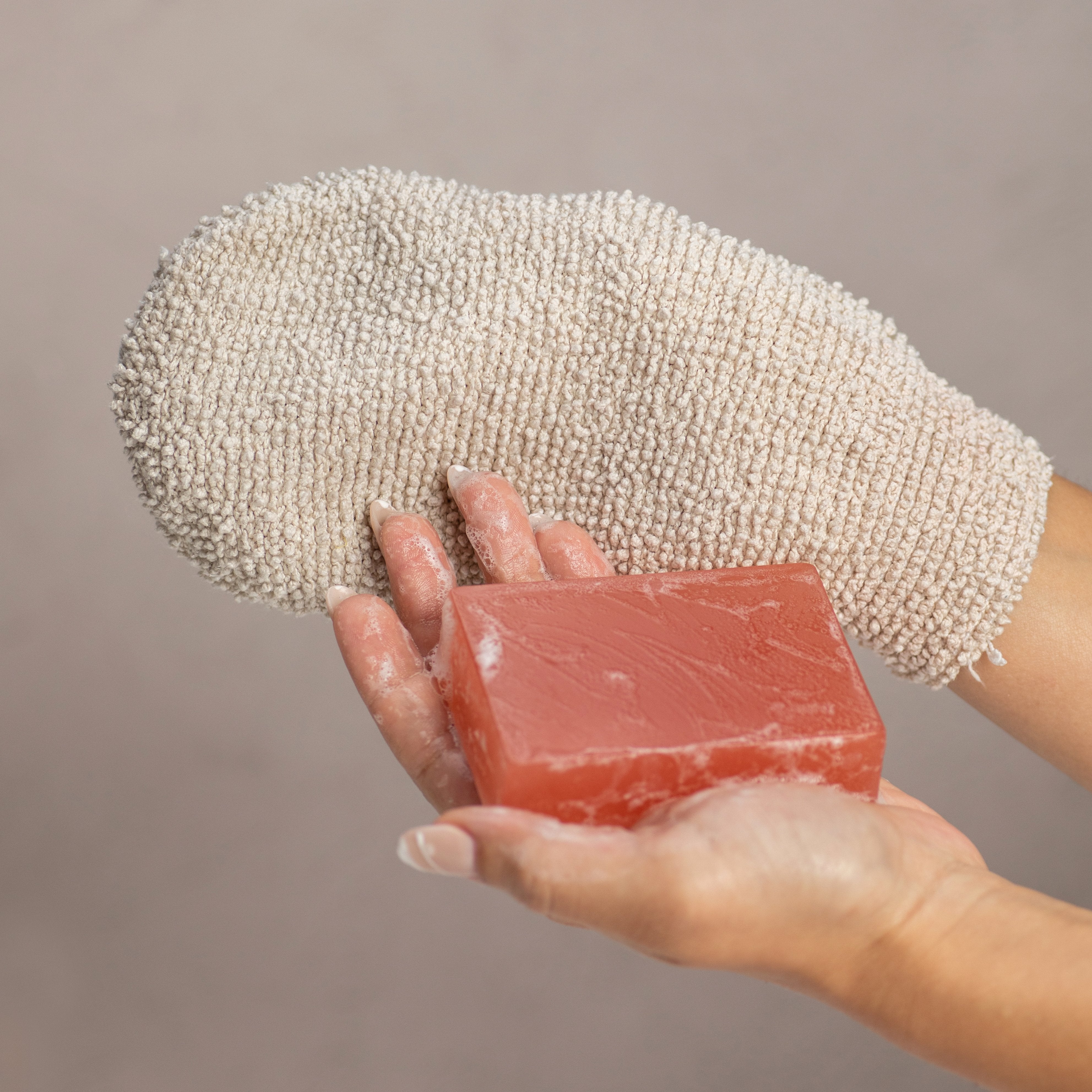 Natural ramie exfoliating bath glove holding red soap, ideal for gentle skin cleansing and circulation stimulation.