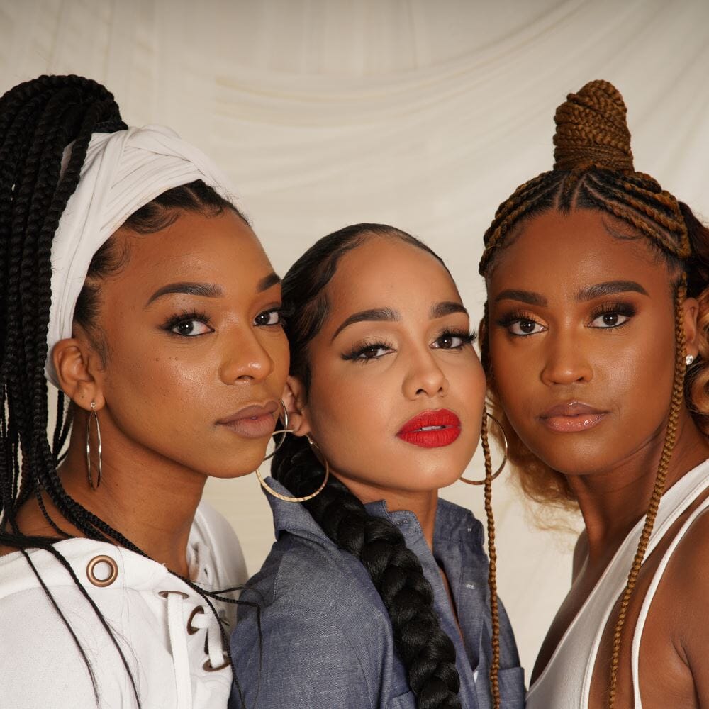 Three women showcasing diverse braided hairstyles with 28" hypoallergenic braiding hair, wearing stylish outfits and hoop earrings.