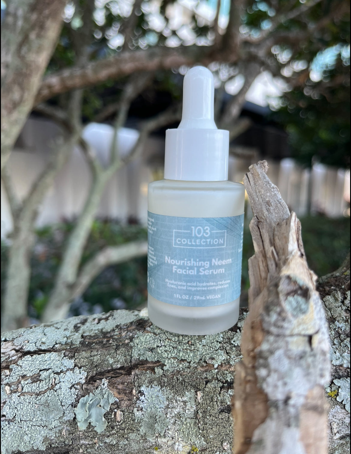 Vegan Nourishing Neem Facial Serum bottle on tree log, moisturizing and protecting skin with Niacinamide, Hyaluronic Acid, Neem.