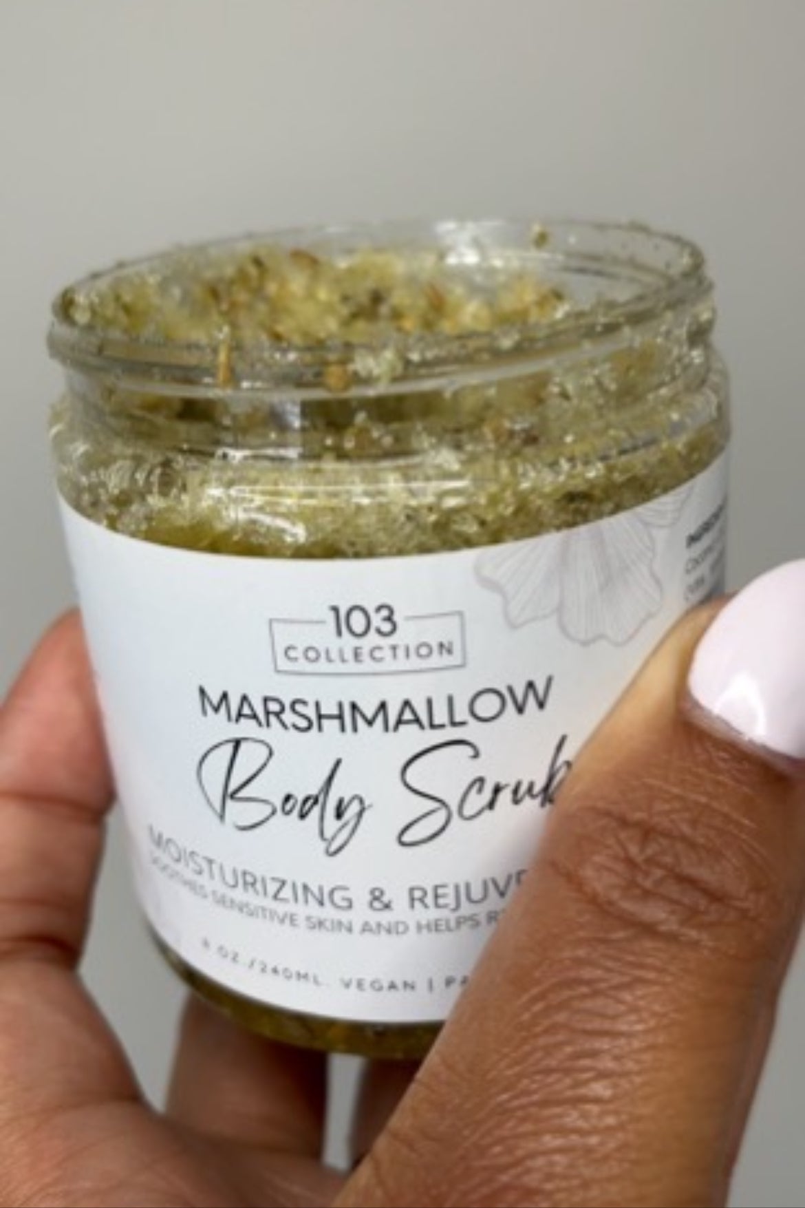 Hand holding a jar of Marshmallow Body Scrub by 103 Collection, a moisturizing and rejuvenating skincare product for sensitive skin.