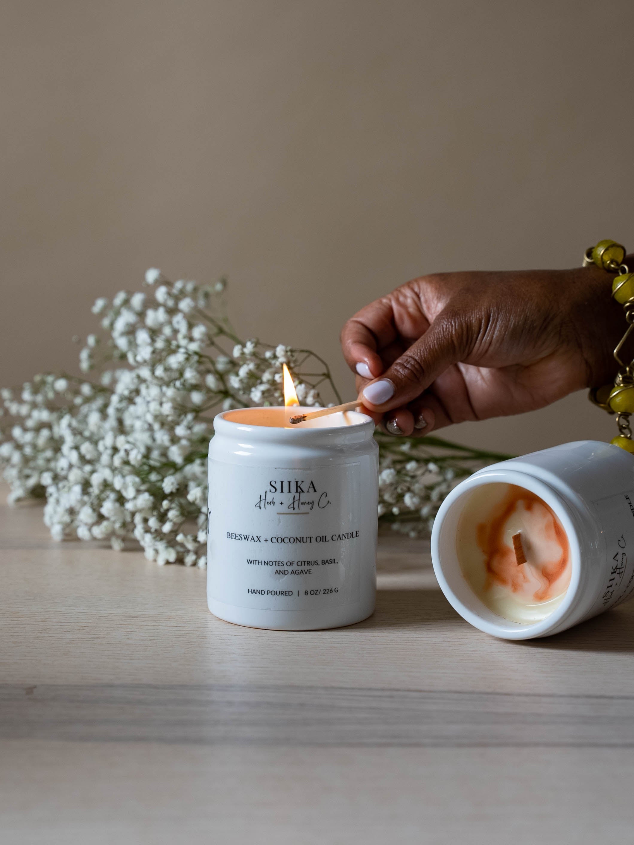 Hand lighting Warm Vanilla & Coconut beeswax candle with flowers in background