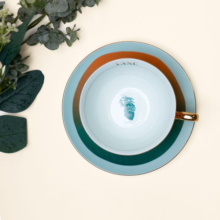Top view of Haint Blue Tea Set cup and saucer with ombré finish, symbolizing Gullah-Geechee heritage, next to eucalyptus leaves.