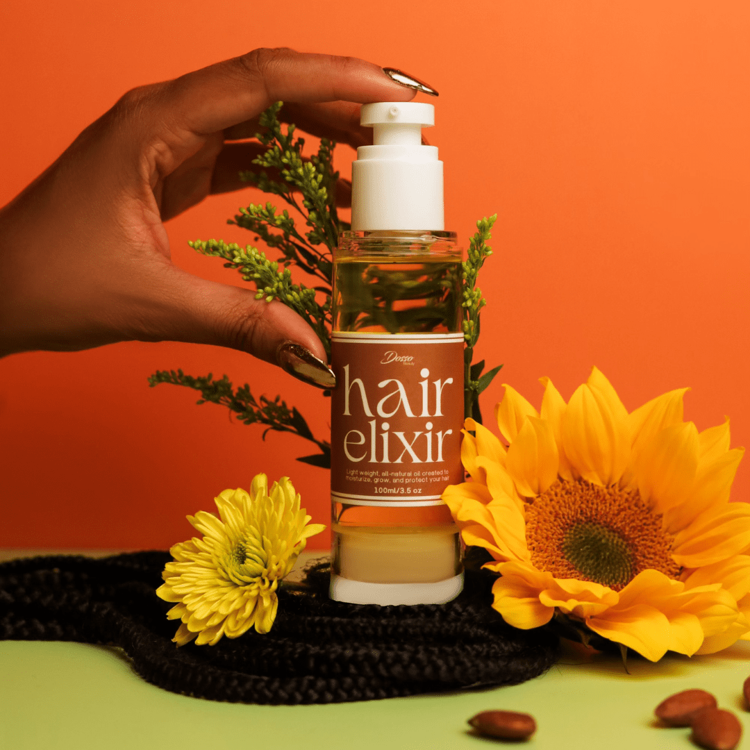 Hand holding Dosso Beauty Hair Elixir bottle with sunflowers, featuring natural oils like Jojoba and Vitamin E for nourishing hair care.