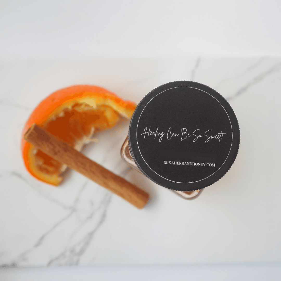Top view of Renee Anastasia Orange Spice Honey jar with orange slice and cinnamon stick on marble surface.