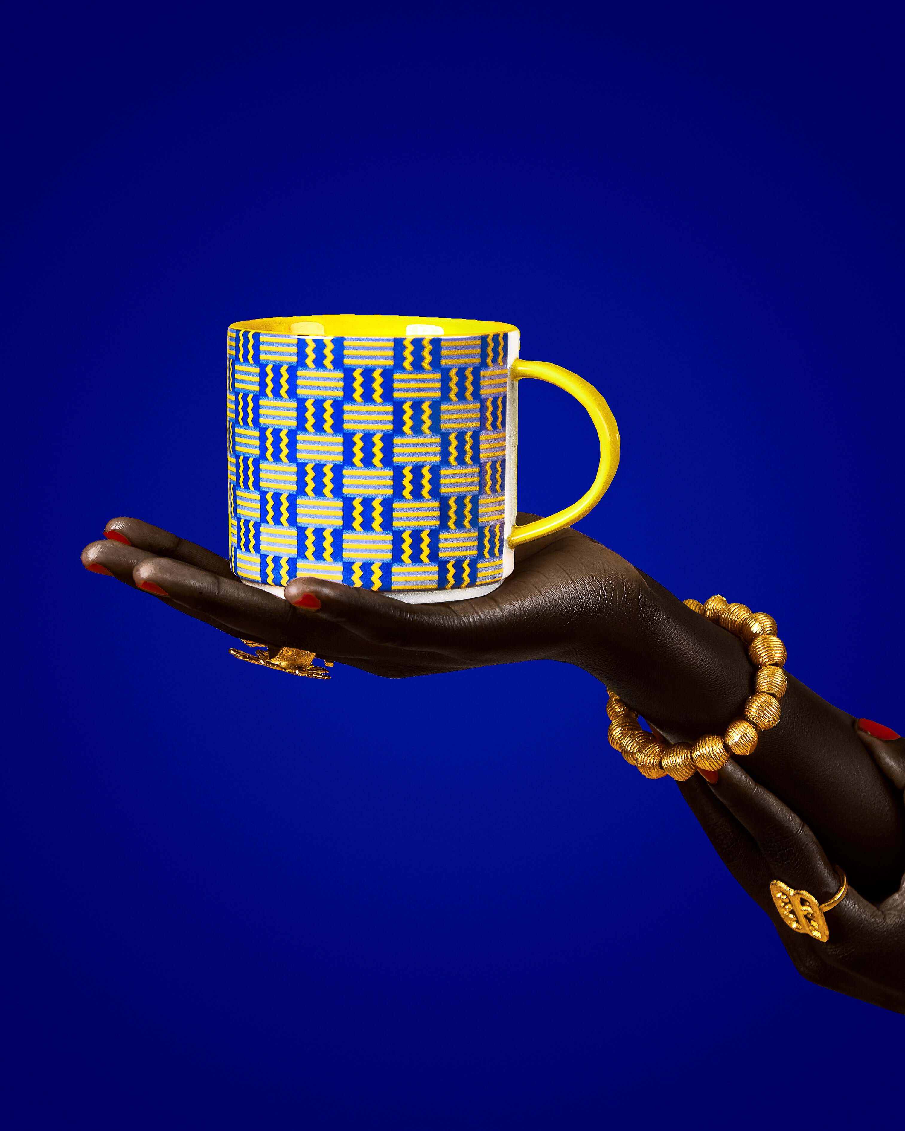 Kente-inspired mug held in a hand, showcasing vibrant yellow and blue patterns symbolizing prosperity and unity.
