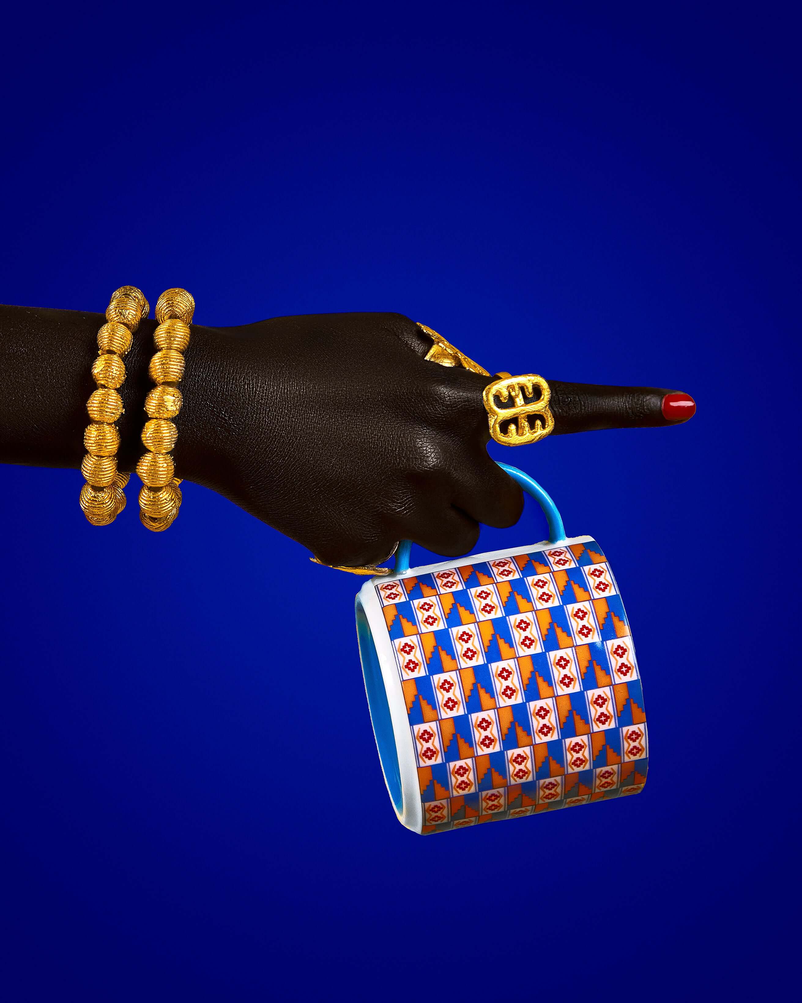 Hand holding a colorful Kente-inspired mug against a blue backdrop, celebrating growth, femininity, and wealth.